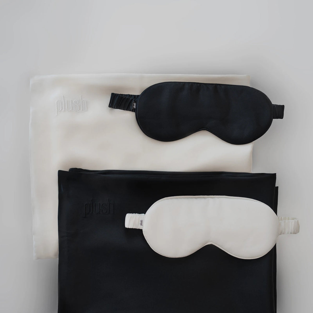 Black and cream silk sleep masks placed on folded silk pillowcases in contrasting colors.