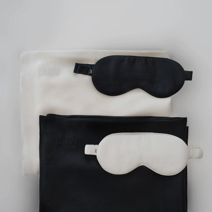 Black and cream silk sleep masks placed on folded silk pillowcases in contrasting colors.